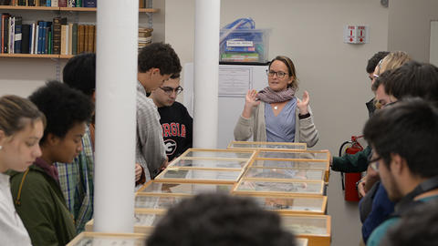 a person teaching students, standing around a table with boxes of insect specimens