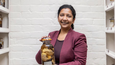 a person smiling at the camera, holding a glass jar of museum specimens