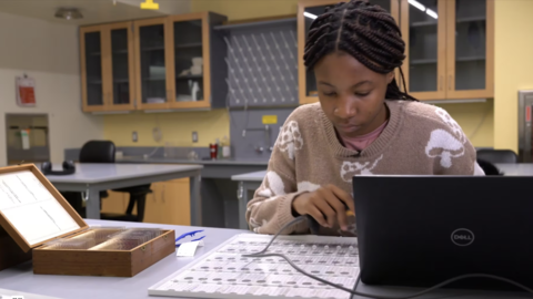 a person at a laptop working on a tray of glass slides