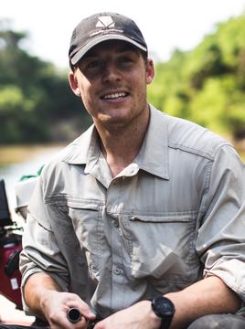 a person smiling at the camera, outside with green foliage in the background
