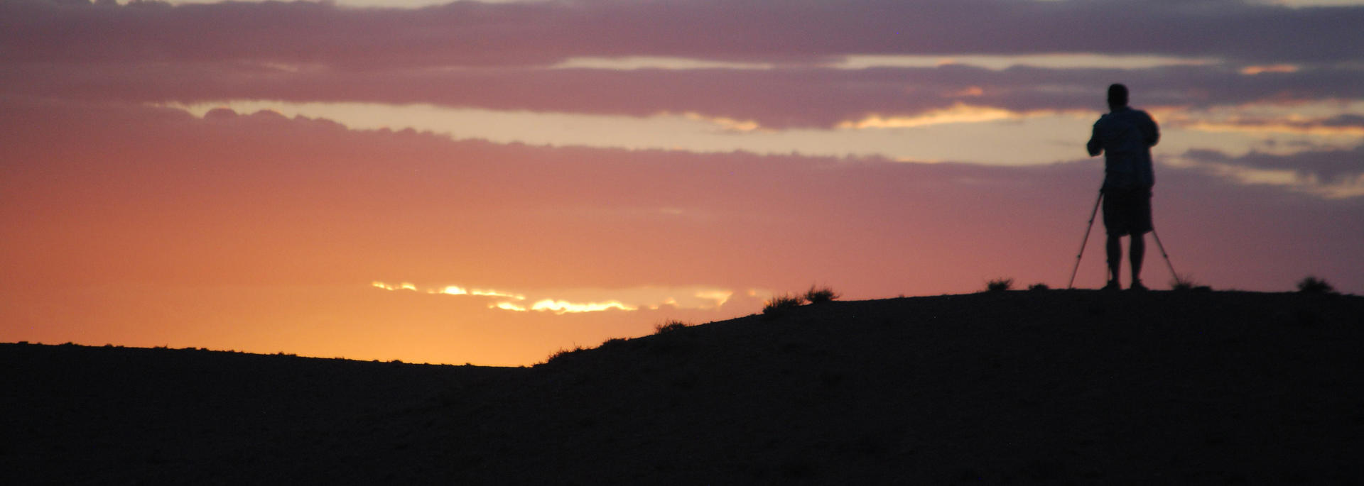 person in silhouette taking a photo of a sunset