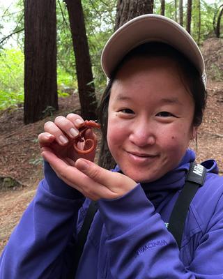 a person holding a small amphibian, standing outside