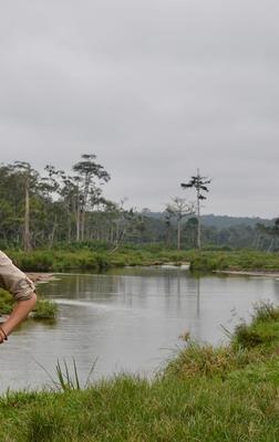 a person standing in front of a river and green foliage