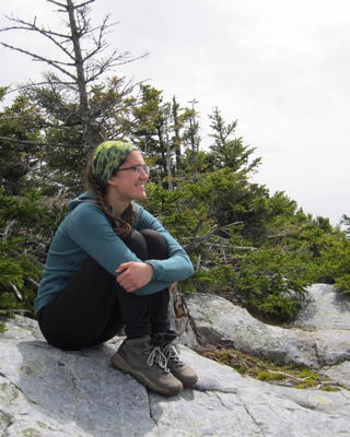 a person sitting on rock, with short trees in the background