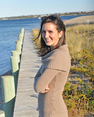 a person smiling at the camera with an ocean, boardwalk, short vegetation background