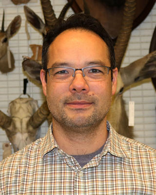 a person looking at the camera, with mounted mammal specimens in the background