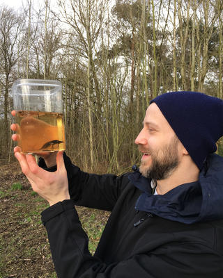 a person outside holding a jar with liquid and a salamander