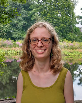 a person smiling at the camera, with a pond and foliage background
