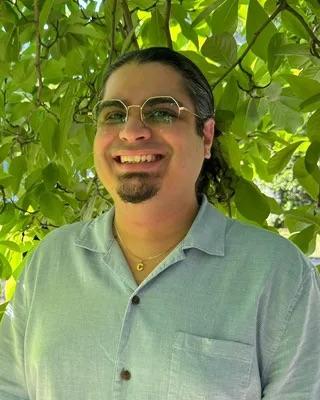 a person smiling at the camera, in front of green foliage