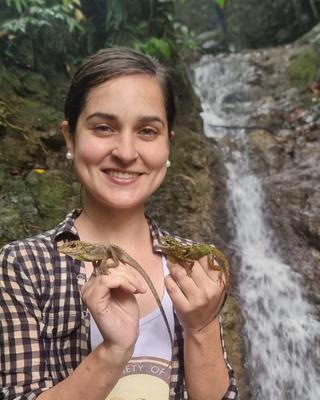 a person in front of a waterfall, holding two lizards