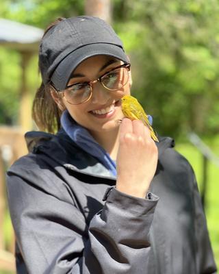 a person standing outside, holding a small yellow bird