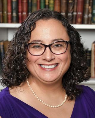 a person smiling at the camera, in front of a bookcase