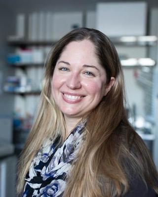 a person smiling at the camera, in a laboratory