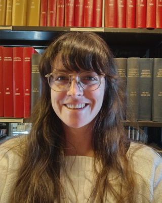 a person smiling at the camera, in front of a full bookcase