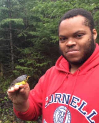 a person looking at the camera, holding a small bird, with green foliage in the background