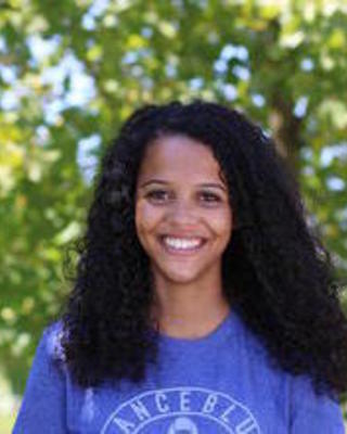 a person smiling at the camera, with a tree in the background