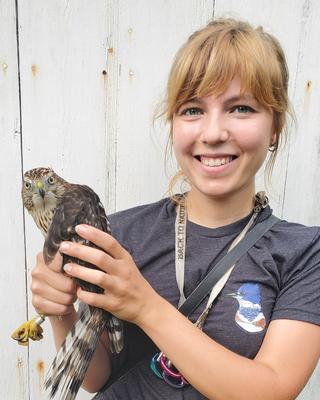 a person smiling at the camera, holding a large bird of prey
