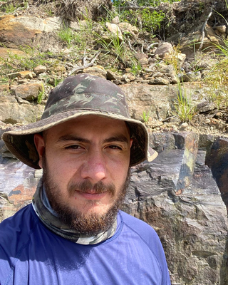 a person standing outside, with a rock wall and vegetation background
