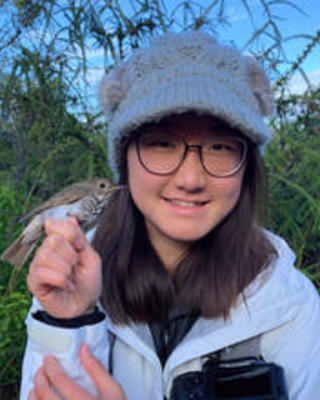 a person outside, holding a small bird