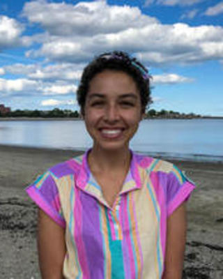 A person smiling at the camera, on a beach