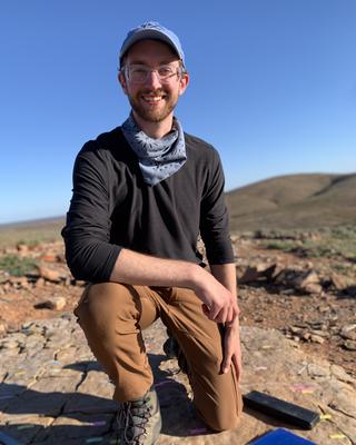 a person in a desert, kneeling and smiling at the camera.