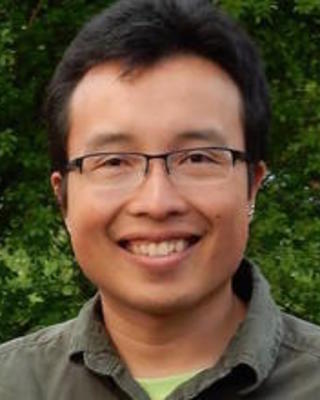 a person smiling at the camera, in front of dark green foliage