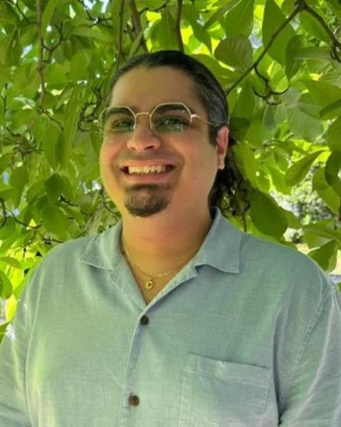 a person smiling at the camera, in front of green foliage