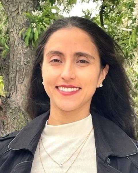 a person smiling at the camera, with trees in the background