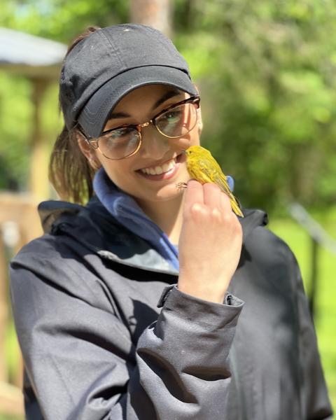 a person standing outside, holding a small yellow bird