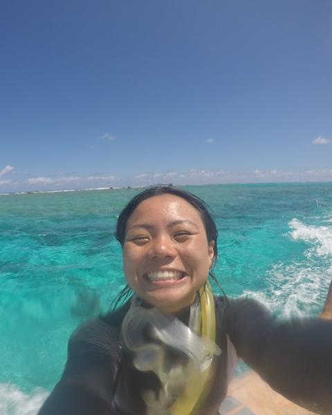 a person smiling at the camera, on a boat with turquoise water and blue sky