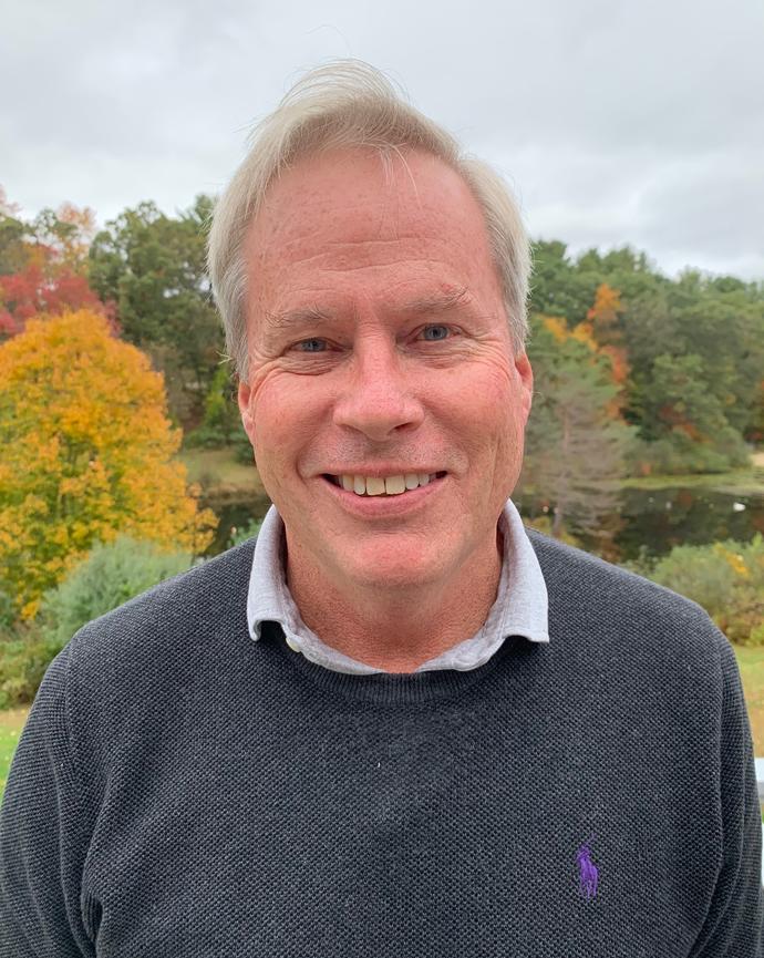 a person standing outside with green and yellow foliage in the background