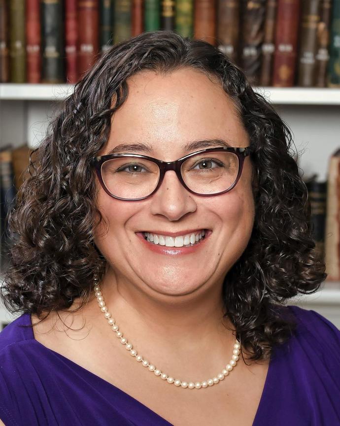 a person smiling at the camera, in front of a bookcase
