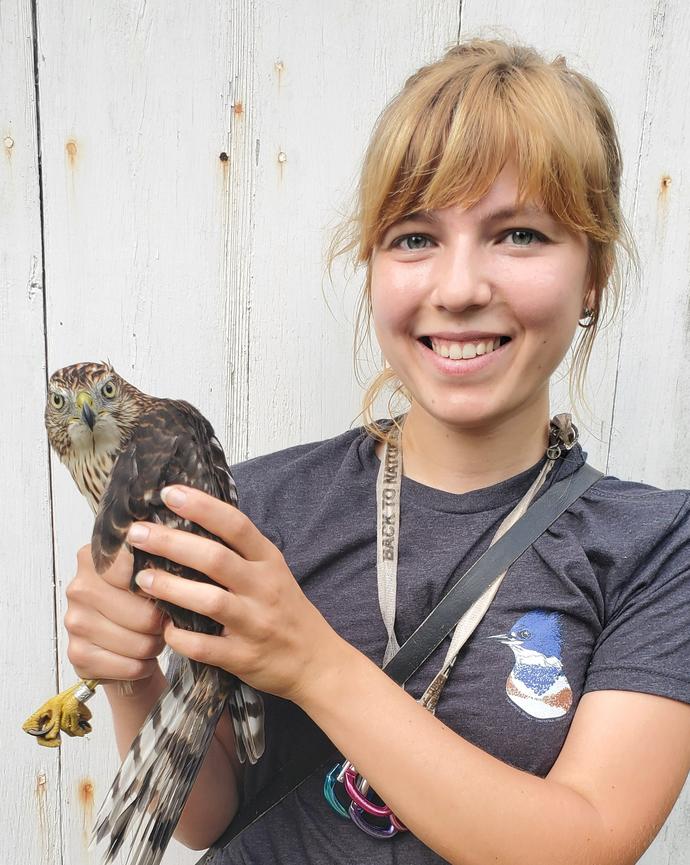 a person smiling at the camera, holding a large bird of prey